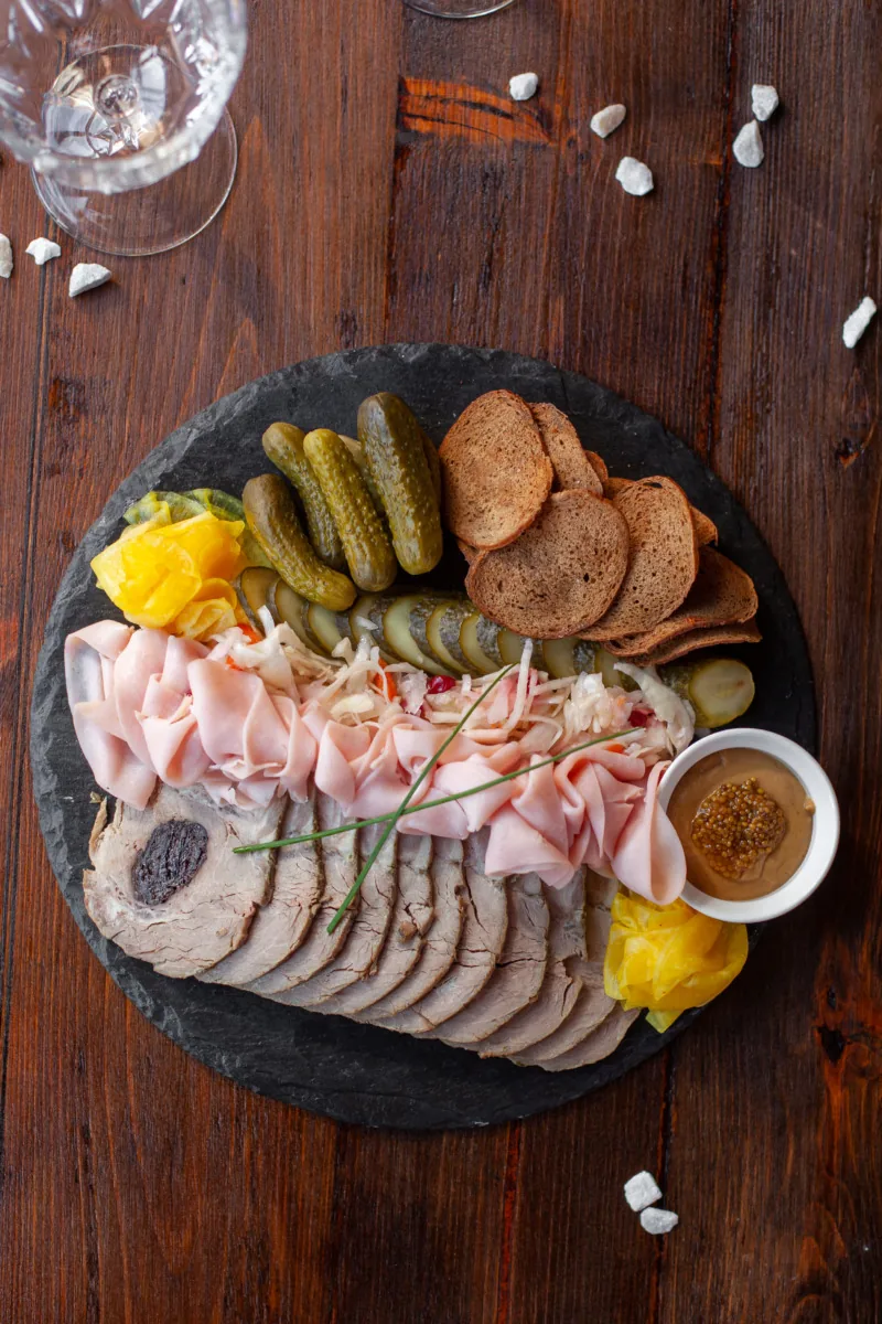 Мясное ассорти с соленьями и тостами на тёмном блюде